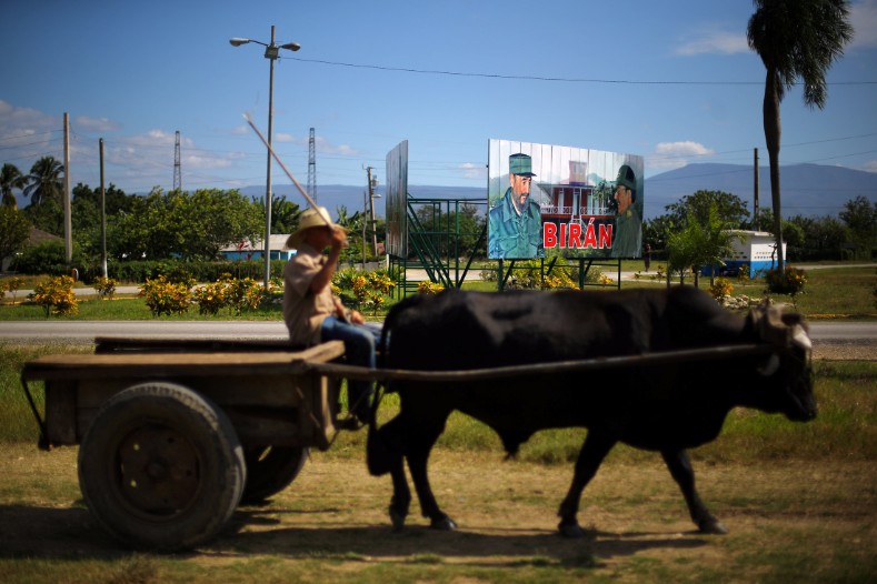 An oxcart drives past a sign showing photographs of Cuba's former President Fidel Castro and his brother, Cuba's President Raul Castro, in Biran.