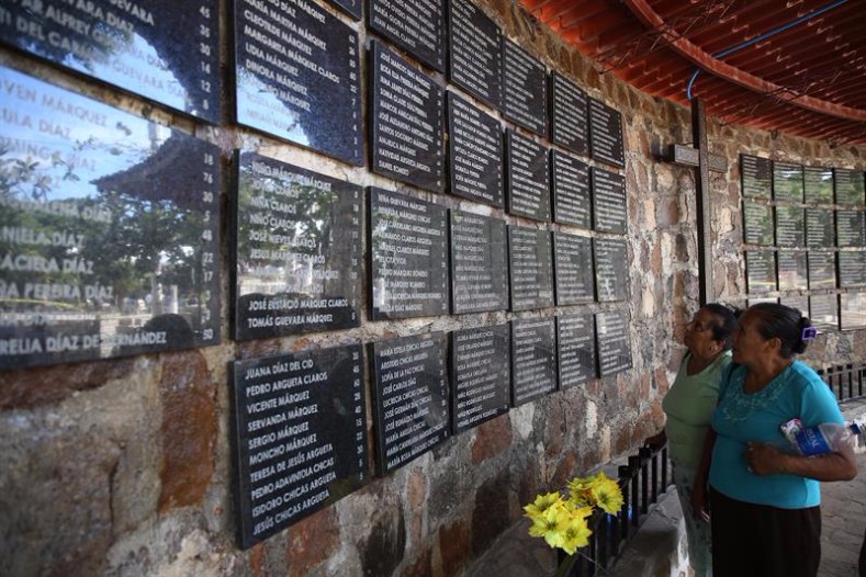 Women read the names of the victims of the El Mozote massacre, displayed on a wall, during the event to commemorate 35 years since the tragic act.