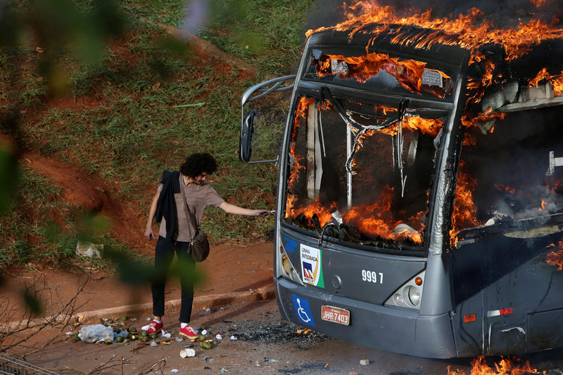 A man lights up his cigarette with the flames of a burning bus.