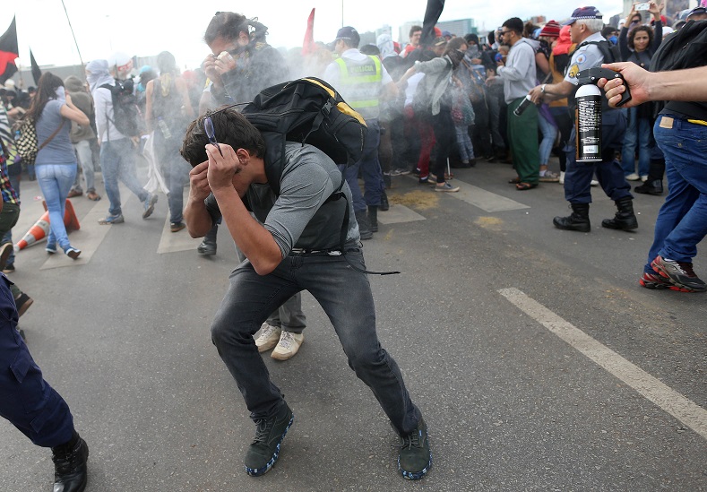 A riot-policeman fires pepper spray against a demonstrator during a protest against the constitutional amendment PEC 55, which limits public spending.