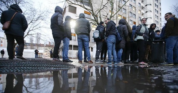 Migrants and refugees are reflected in a puddle as they queue in front of the compound of the Berlin Office of Health and Social Affairs (LAGESO) for their registration process, early morning in Berlin, Germany, Feb. 2, 2016.