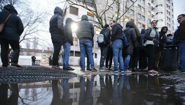Migrants and refugees are reflected in a puddle as they queue in front of the compound of the Berlin Office of Health and Social Affairs (LAGESO) for their registration process, early morning in Berlin, Germany, Feb. 2, 2016.