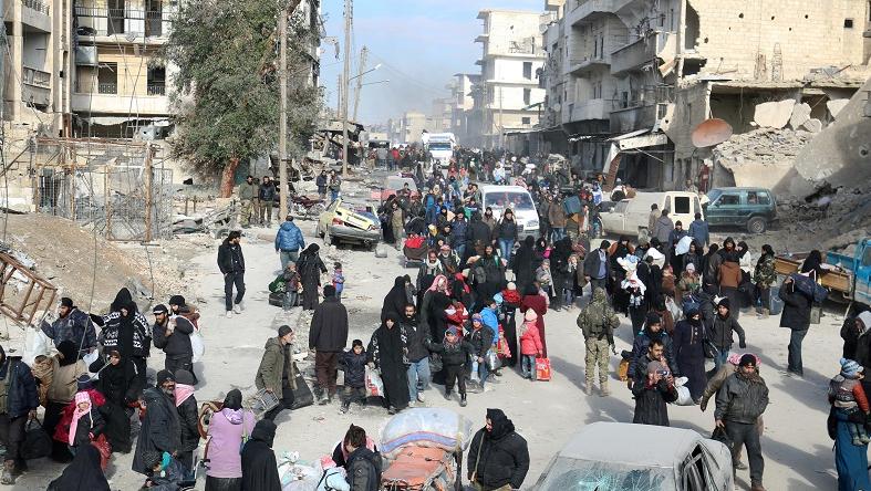 Rebel fighters and civilians gather near damaged buildings as they wait to be evacuated from a rebel-held sector of eastern Aleppo, Syria December 18, 2016.