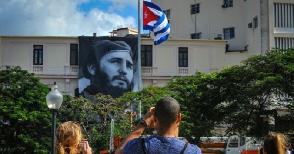 A Cuban flag flutters at half mast near a banner depicting Cuban revolutionary leader Fidel Castro in Havana.