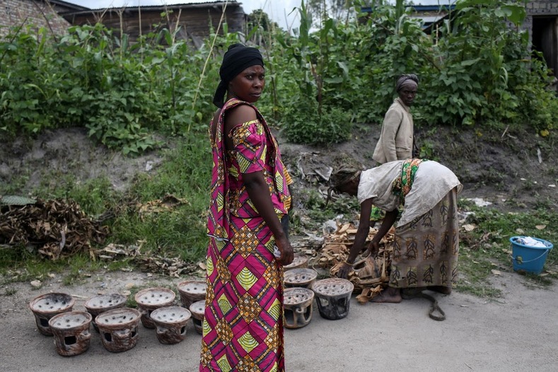 A Bahavu woman stands (L) as Pygmy women sell pottery in the Bahavu village of Bugarula on Idjwi island. The Bambuti lost their livelihood and, with few if any assets, no education, and no experience of how to support themselves in an alien environment, their society has withered.