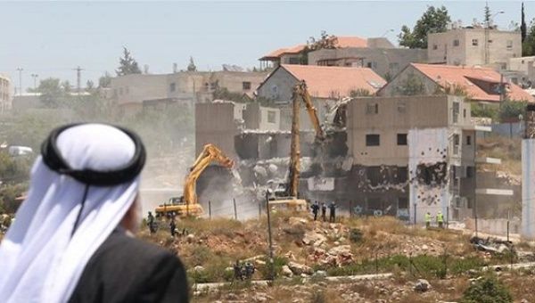 A Palestinian man watches Israeli heavy machinery demolish apartment blocs in the occupied West Bank settlement of Beit El, July 29, 2015.