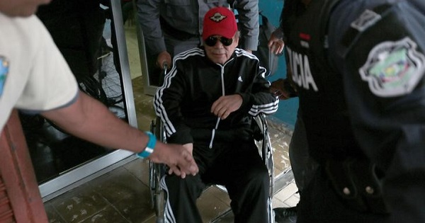 Former Panamanian dictator Manuel Noriega sits in a wheelchair as prison wardens help him after a health check up at the facilities in Panama City.