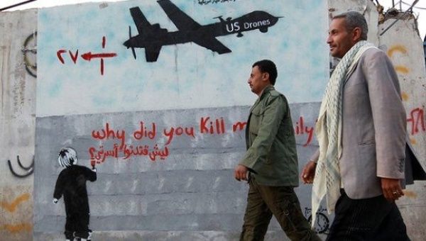 Yemeni men walk past a mural depicting a US drone and reading 'Why did you kill my family,' in the capital, Sanaa.