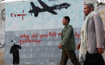 Yemeni men walk past a mural depicting a U.S. drone, which reads, 