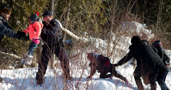Royal Canadian Mounted Police officers assist a child from a family that claimed to be from Sudan as they walk across the U.S.-Canada border.