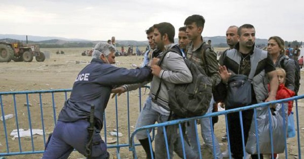 A policeman pushes refugees behind a barrier at Greece's border with Macedonia, near the village of Idomeni, Greece.