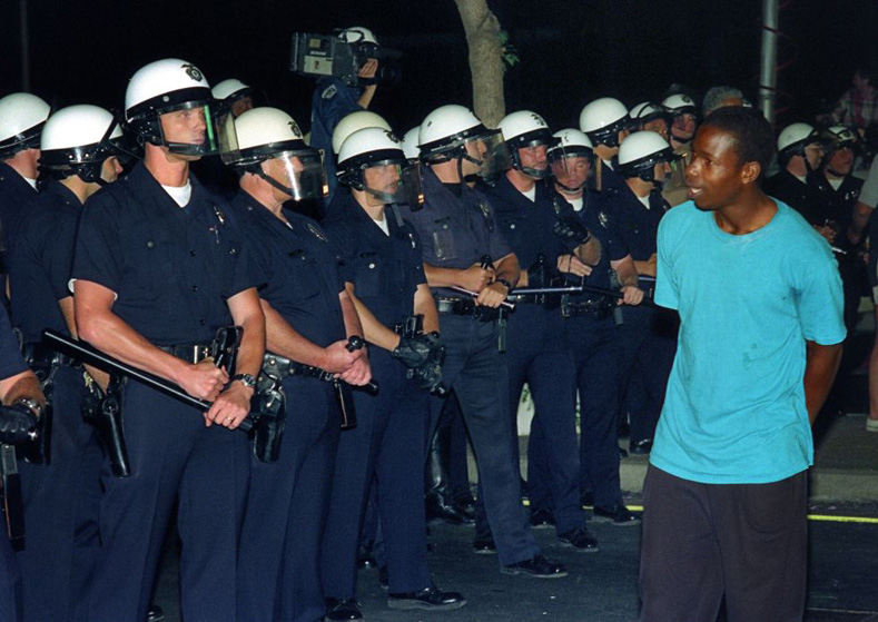 A local resident walks past a line of Los Angeles police officers on April 30, shortly before community rage exploded.