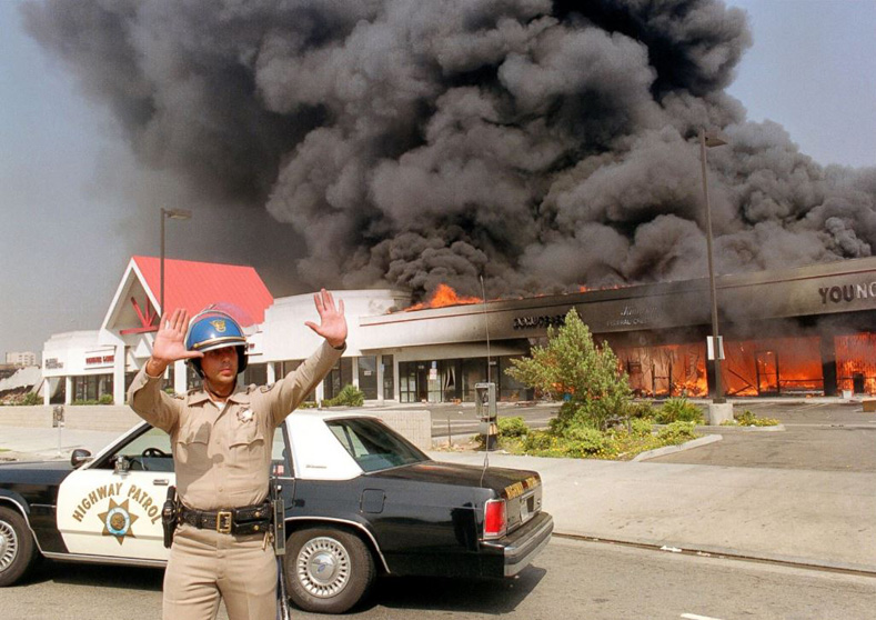 A California Highway patrolman directs traffic around a shopping center engulfed in flames on April 30, 1992, in Los Angeles.