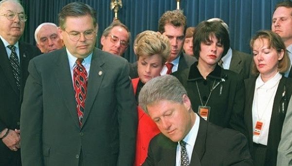 Clinton signs law with right-wing congresspeople Ileana Ros-Lehtinen (red), Bob Menendez (next to Clinton), Jesse Helms (far left), and Lincoln Diaz-Balart (back right).