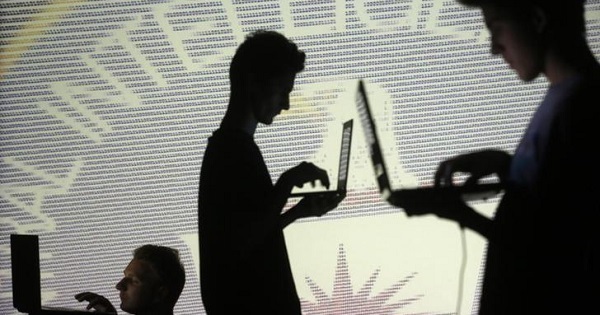People are silhouetted as they pose with laptops in front of a screen projected with binary code and a Central Inteligence Agency (CIA) emblem.
