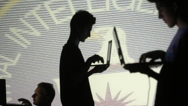 People are silhouetted as they pose with laptops in front of a screen projected with binary code and a Central Inteligence Agency (CIA) emblem. 