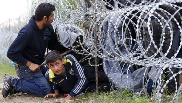 Syrian asylum-seekers climb under rolls of razor wire into Hungary at the border with Serbia.