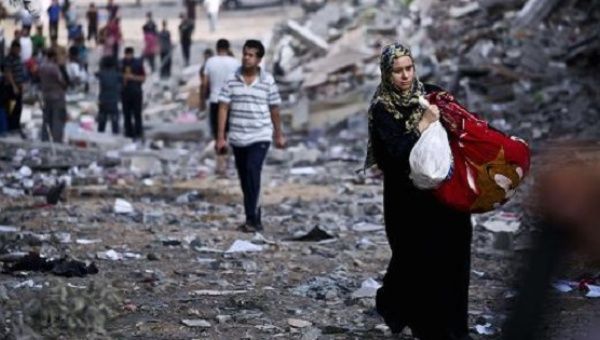 A Palestinian woman takes belongings from her partially destroyed home across the street from where a building was targeted by Israeli airstrikes, Aug. 26, 2014.
