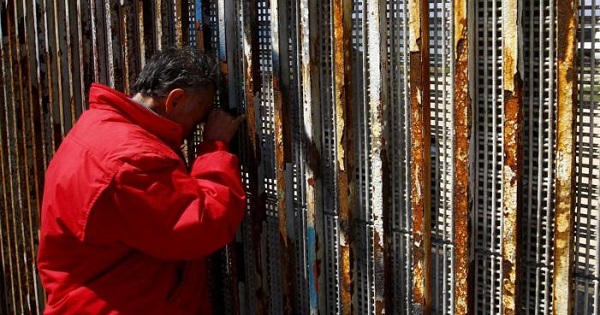 A man talks to relatives at a wall separating Mexico and the United States, as photographed from Playas Tijuana, in Tijuana, Mexico.