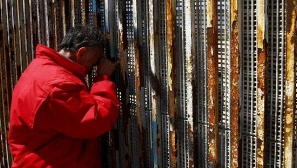  A man talks to relatives at a wall separating Mexico and the United States, as photographed from Playas Tijuana, in Tijuana, Mexico.
