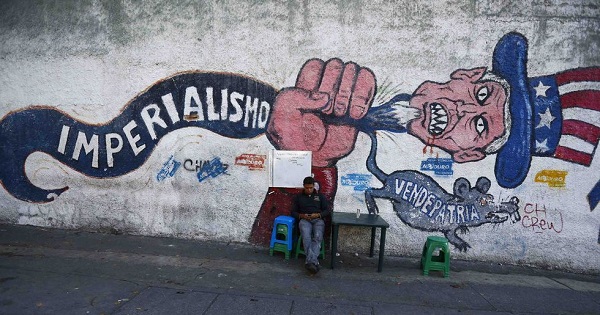 Man sits by a graffiti denouncing U.S. imperialism in Caracas.