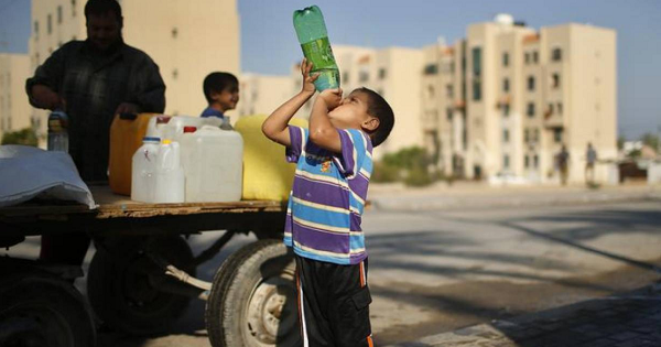 A Palestinian boy drinks water next to a cart loaded with containers filled with water from public taps in the northern Gaza Strip, June 20, 2013.