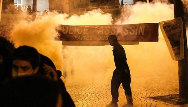 Anti-riot police throw tear gas as a man stand next to a banner reading 