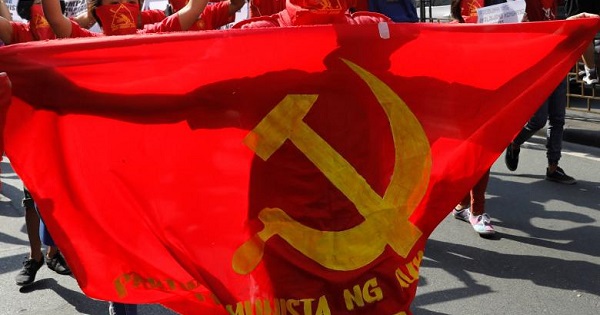 A protester stands behind a Communist sickle and hammer banner as members and supporters of a Communist movement march along a street in Manila.