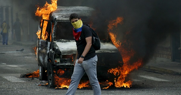 An opposition protester wearing a Venezuelan national flag to cover his face walks in front of a burning van during a protest against President Nicolas Maduro's government.