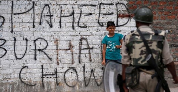 A boy stands next to a wall painted with graffiti as a policeman stands guard during a protest in Srinagar, Kashmir.
