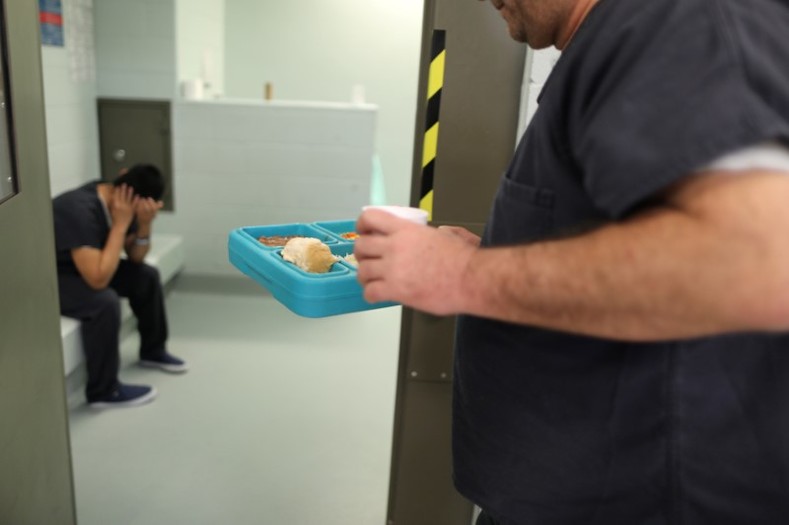 An immigrant takes food into a cell for incoming ICE detainees at the Adelanto immigration detention center, which is run by the Geo Group Inc. The  owns, leases and manages correctional and detention facilities across the country.