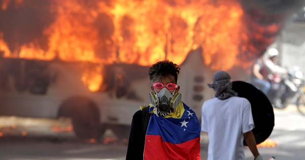 A protesters stands in front of a burning bus during protests in Caracas.