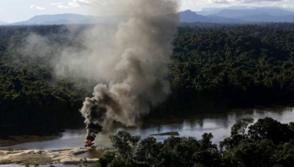 An illegal gold dredge is seen burning down at the banks of Uraricoera River during Brazil’s environmental agency raid in the Amazon.