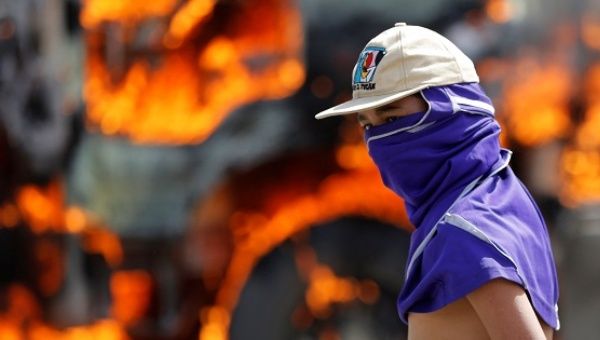 A demonstrator looks on as a truck set on fire to build a barricade burns in the background in a protest in Caracas.