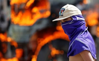 A demonstrator looks on as a truck set on fire to build a barricade burns in the background in a protest in Caracas.