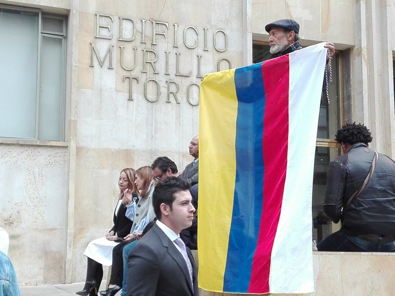 A man holds the Colombian flag with an extra white stripe added to represent peace. 