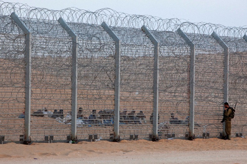 An Israeli soldier stands near the border fence between Israel and Egypt as African would-be immigrants sit on the other side near the Israeli village of Be'er Milcha September 6, 2012.