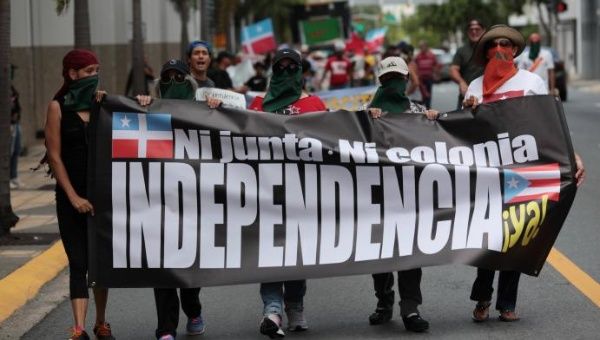 Puerto Ricans march in support of becoming an independent nation. The sign reads 'Neither (Financial Oversight and Management) Board, Nor Colony, Independence Now!'
