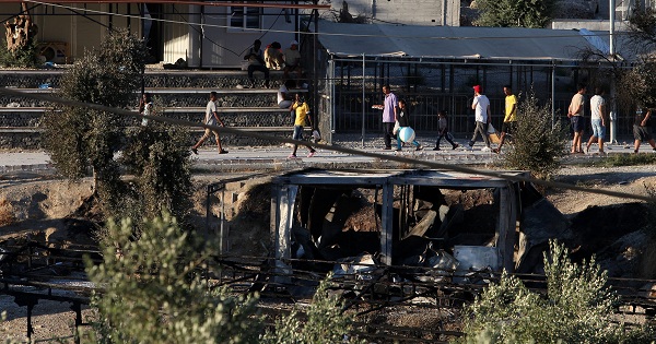 Migrants walk next to debris of burned shelters at the Moria refugee camp on the island of Lesbos, Greece, on July 10, 2017.