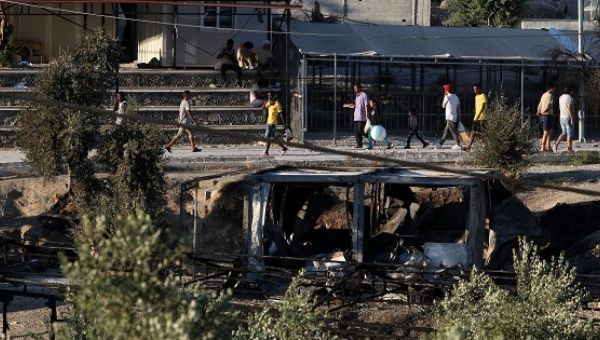 Migrants walk next to debris of burned shelters at the Moria refugee camp on the island of Lesbos, Greece, on July 10, 2017. 
