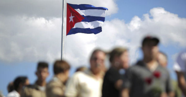 Cubans passing in front of the national flag.