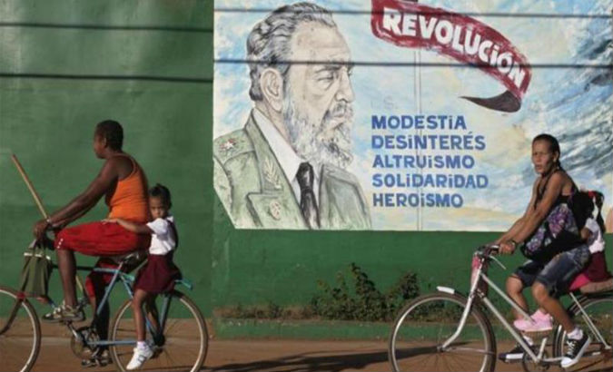 Cubans bicycle pass an image of Fidel Castro which says: 
