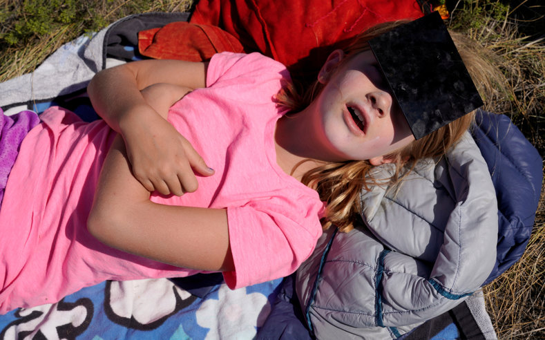 In Guernsey Wyoming Jessica Loy lies on the grass covered in sunblock and wearing welders glasses to view the eclipse.