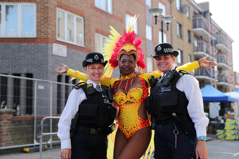 A woman in costume poses with two members of London's Metropolitan Police. The Met has been heavily criticized for the institutionalized racism evident in the way their approach to the policing of Notting Hill.