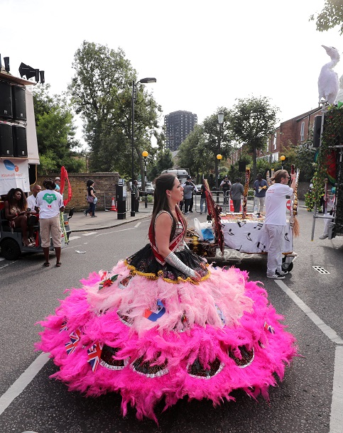 A woman in costume makes her way along the Notting Hill parade route. The burnt out shell of the Grenfell Tower block is visible in the background.