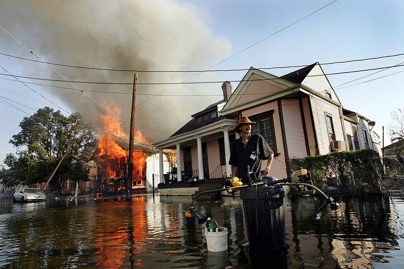 A man stands in floodwaters as fire burns down a home in the seventh ward of New Orleans in the aftermath of Hurricane Katrina.