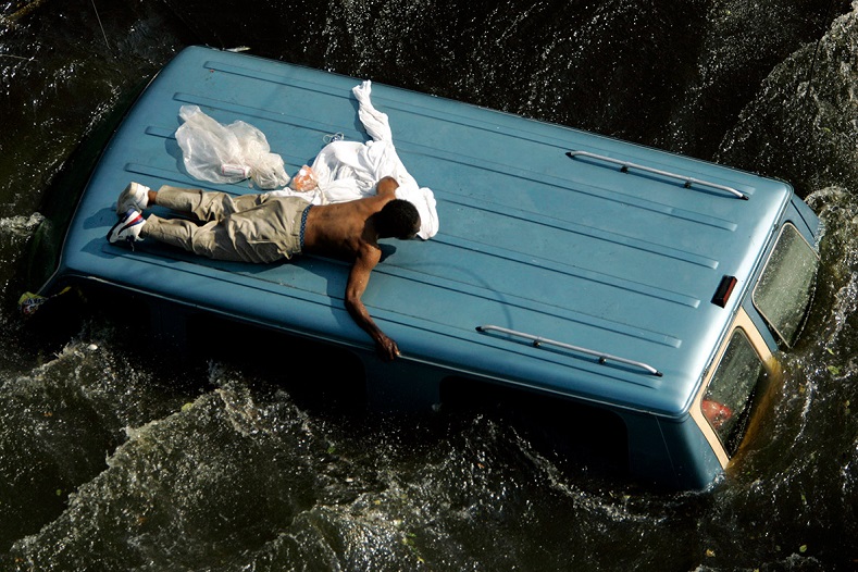 A man clings to the top of a vehicle before being rescued by the U.S. Coast Guard from the flooded streets of New Orleans, in the aftermath of Hurricane Katrina, in Louisiana. 