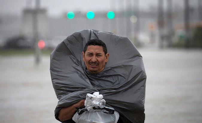 A man uses a trash bag as cover from the rain while wading through floodwaters in east Houston, Texas.