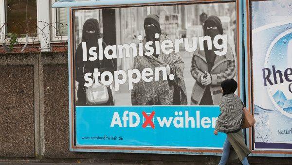 A woman with a headscarf walks past an election campaign poster of the anti-immigration party Alternative for Germany, AfD, in Marxloh, a suburb of Duisburg which local media said is populated mostly with people of Turkish migrant background, Germany, Sept. 13, 2017.