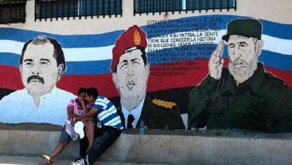 A couple sits in front of a mural depicting Nicaragua’s President Daniel Ortega, Venezuela’s Hugo Chavez, and Cuba’s Fidel Castro in Managua.
